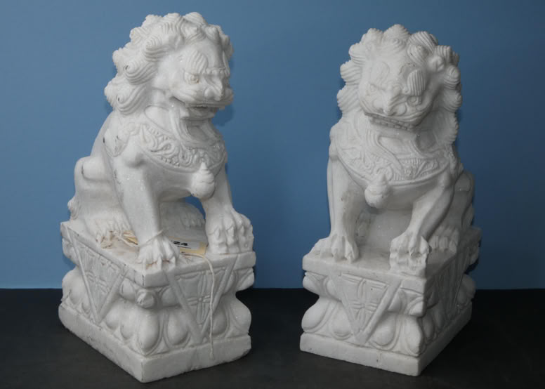 Two white stone lion statues on ornate rectangular bases against a blue background.